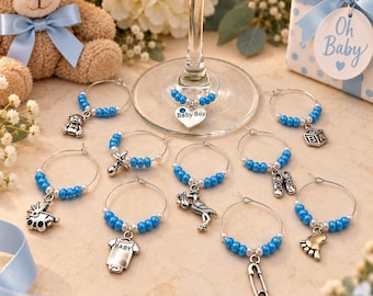 May include: A set of ten silver-toned wine glass charms featuring baby-themed metal pendants including a teddy bear, baby shoes, a stork, a pacifier, a safety pin, a baby carriage, a onesie with the word BABY, and a heart charm labeled Baby Boy.