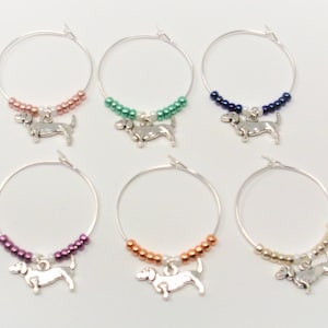 May include: Six silver wine glass charms with dachshund charms. Each charm has a different color of beads: pink, green, blue, purple, orange, and gold.