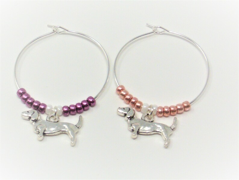 May include: Two silver wine glass charms with dachshund charms. One charm has a purple and white beaded chain, the other has a copper and white beaded chain.