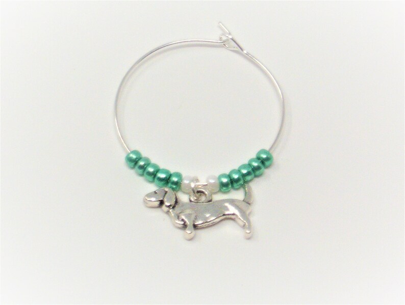 May include: A silver charm of a dachshund dog hanging from a silver wire hoop with green and white beads.