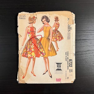 May include: Vintage McCall's sewing pattern for misses' and junior dresses. The pattern cover features illustrations of three dresses in floral and solid fabrics. The pattern number is 6722, and the size is 13 with a 33-inch bust.