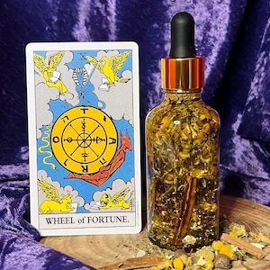 Könnte beinhalten: Eine Tarotkarte, die das Rad des Schicksals mit einem goldenen Rad, einer Sphinx und zwei geflügelten Kreaturen zeigt. Im Vordergrund befindet sich eine Glasflasche, gefüllt mit Kräutern und Gewürzen, darunter Zimtstangen.