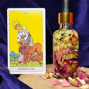 Puede incluir: Una botella de vidrio llena de flores secas y una carta de tarot que representa la carta de la Fuerza de la baraja Rider-Waite. La carta muestra a una mujer con una corona de flores, sosteniendo suavemente la mand&iacute;bula de un le&oacute;n abierta. El texto de la carta dice "VIII FUERZA."