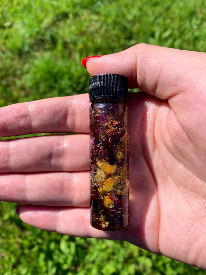 May include: A small glass bottle filled with a clear liquid and dried flowers. The bottle has a black screw-on cap.