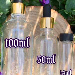 Puede incluir: Tres botellas de vidrio con tapas doradas y goteros. Las botellas son transparentes y tienen etiquetas con el texto "100ml", "50ml" y "14ml" en una fuente g&oacute;tica.