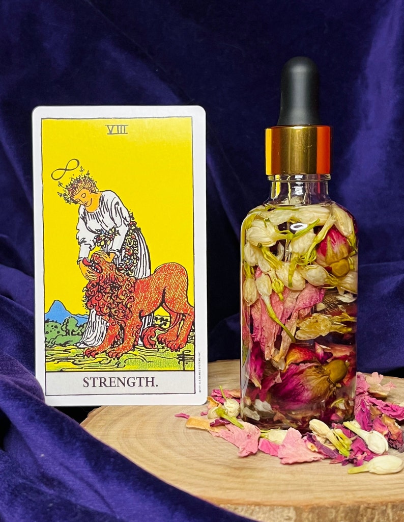 Puede incluir: Una botella de vidrio llena de flores secas y una carta de tarot que representa la carta de la Fuerza de la baraja Rider-Waite. La carta muestra a una mujer con una corona de flores, sosteniendo suavemente la mand&iacute;bula de un le&oacute;n abierta. El texto de la carta dice "VIII FUERZA."