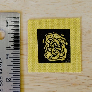 May include: A yellow fabric patch with a black square containing a black and white abstract design.
