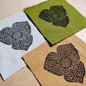 Può includere: Tre quadrati di tessuto con un motivo floreale nero stampato su di essi. I quadrati sono di diversi colori: bianco, beige e verde.
