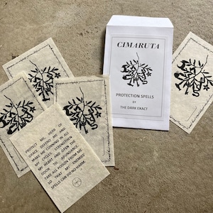 May include: Five white cards with black ink illustrations and text. The cards feature a stylized image of a plant with a key, a snake, and a crescent moon. The text on the cards reads "Protect me, herb of grace. Defend me and make me cunning in all my cycles. Strengthen my heart and open the door to abundance. Take all poison from me so that my enemies' spells can do no harm." The cards are in a white envelope with the text "CIMARUTA Protection Spells by The Dark Exact".