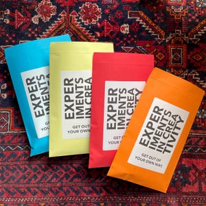 May include: Four colorful envelopes with the text "Experiments in Creativity" and the phrase "Get out of your own way" printed on them.