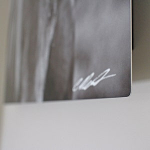 May include: A black and white photograph of a person's torso, with a white signature in the bottom right corner.