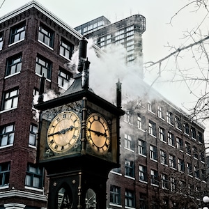 May include: A vintage-style steam clock with two clock faces, set against a backdrop of brick buildings. The clock is emitting steam from its top, creating a whimsical and atmospheric scene.