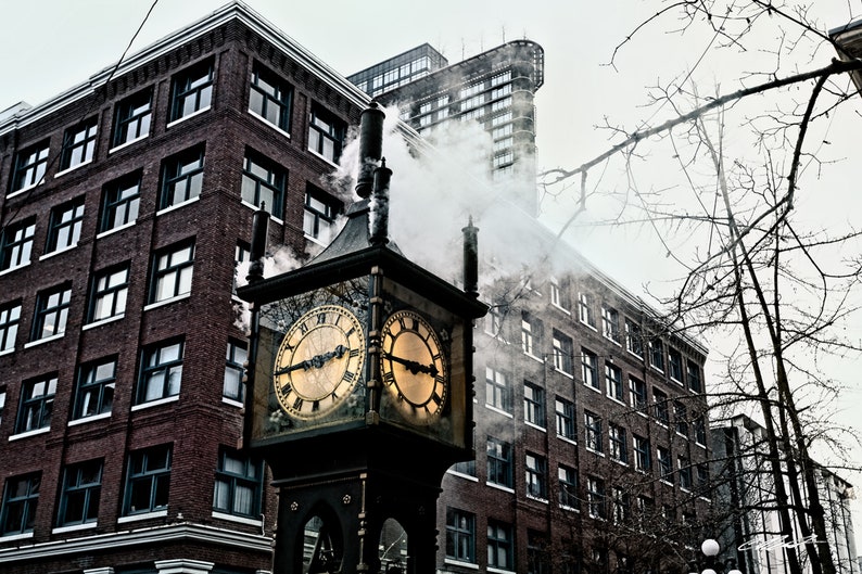 May include: A vintage-style steam clock with two clock faces, set against a backdrop of brick buildings. The clock is emitting steam from its top, creating a whimsical and atmospheric scene.