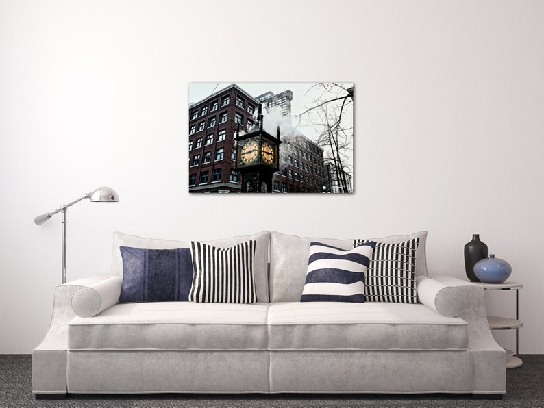 May include: A black and white photograph of a clock tower in a city. The clock tower is made of brick and has a large clock face. The clock tower is surrounded by other buildings. The photo is taken from a low angle, looking up at the clock tower.