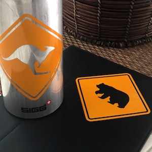 May include: A silver water bottle with a yellow warning sign featuring a kangaroo. A black surface with a yellow warning sign featuring a bear.