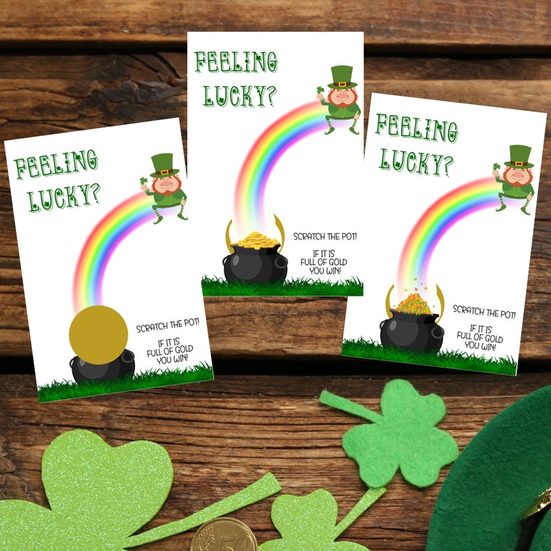 May include: Three St. Patrick's Day scratch-off cards with a rainbow, pot of gold, and leprechaun illustration. The cards read "Feeling Lucky?" and "Scratch the Pot! If it is full of gold you win!" on a wooden background with shamrock decorations.