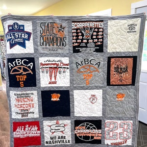 May include: A gray and white quilt made from t-shirts with basketball-themed designs. The quilt features the words "All Star Game", "State Champions", "ArBCA Top 5", "Scrapperettes", "Making History", "All Star Showdown", "We Are Nashville", "Nashville HOCO", "State Champions Scrapperettes", "Finally", "Lauren #4", and "Nashville Homecoming".