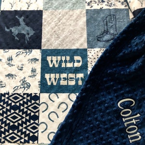 May include: A blue and white patchwork baby blanket with a blue minky backing. The blanket features a variety of western-themed designs, including horses, cowboys, and horseshoes. The blanket is personalized with the name "Colton" embroidered in white on the blue minky backing.