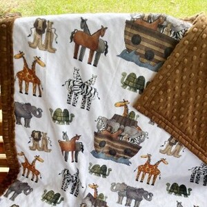 May include: A white and brown baby blanket with a repeating pattern of animals from the Noah's Ark story. The blanket has a brown minky backing.