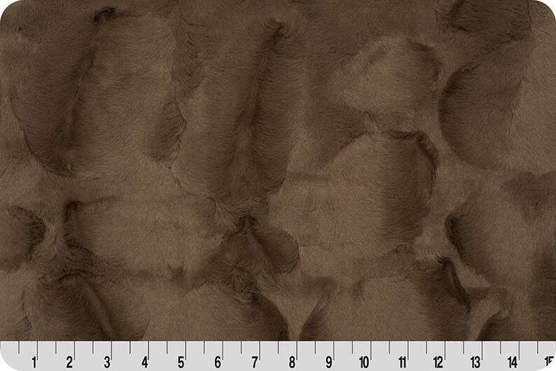 May include: Close-up of a brown faux fur fabric with a soft, plush texture.