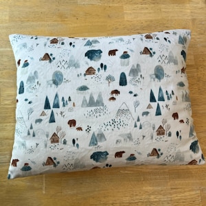 May include: A white pillowcase with a repeating pattern of brown bears, blue mountains, and small houses. The pattern is on a white background.