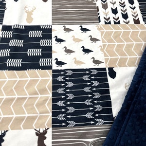 May include: A patchwork baby blanket with a woodland theme. The blanket features a variety of patterns, including deer, ducks, arrows, and wood grain. The blanket is made of soft, comfortable fabric and is perfect for cuddling.