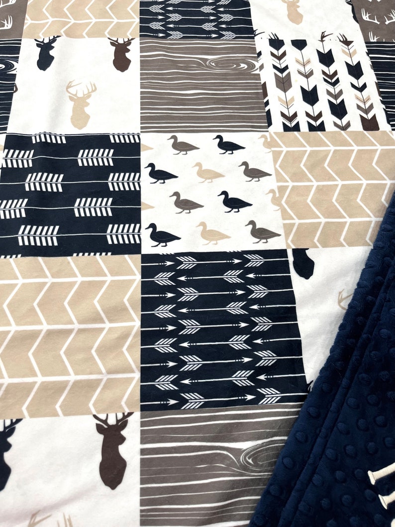 May include: A patchwork baby blanket with a woodland theme. The blanket features a variety of patterns, including deer, ducks, arrows, and wood grain. The blanket is made of soft, comfortable fabric and is perfect for cuddling.
