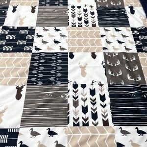 May include: A patchwork baby blanket with a variety of woodland animal and arrow designs in shades of brown, white, and navy blue.