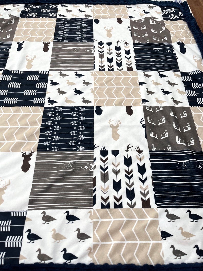 May include: A patchwork baby blanket with a variety of woodland animal and arrow designs in shades of brown, white, and navy blue.