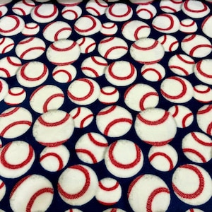 May include: A dark blue fabric featuring a repeating pattern of white baseballs with red stitching. The baseballs are scattered across the surface in various sizes and orientations, creating a dense, uniform graphic print throughout the material.