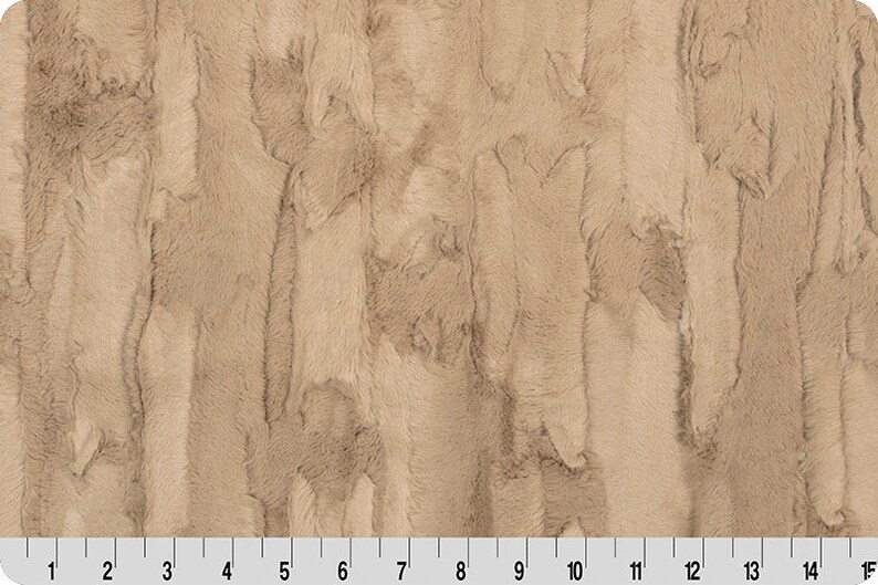 May include: A close-up of a beige faux fur fabric with a vertical striped pattern. The fabric has a soft, plush texture.