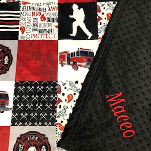 May include: A red, white, and black patchwork quilt with a firefighter theme. The quilt features images of fire trucks, axes, and a firefighter silhouette. The quilt is personalized with the name "Maceo" embroidered on the black side.