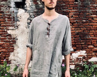 Puede incluir: Túnica de lino gris con cuello redondo y tres botones marrones. La túnica tiene mangas largas remangadas hasta los codos y dos bolsillos delanteros. Se completa con pantalones cortos blancos, para un look relajado.