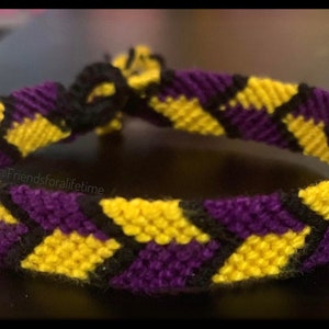 May include: A friendship bracelet with a checkered pattern in yellow, purple, and black colors. The bracelet is tied in a knot and the text "@Friendsforalifetime" is visible.