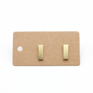 Könnte beinhalten: Ein Paar goldene Barren-Ohrstecker auf einer braunen Karte.