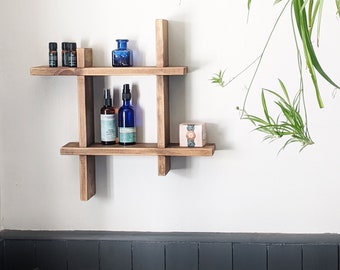 May include: A wooden shelf unit with four shelves, featuring a blue glass bottle and several smaller bottles, a small box, and a plant hanging from the ceiling.