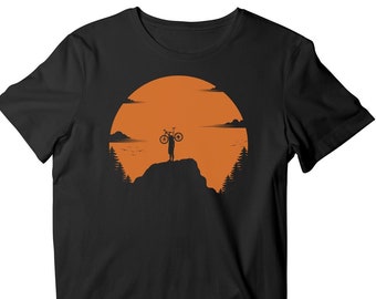 May include: A black t-shirt with a silhouette of a person holding a bicycle on a mountaintop against a sunset background.