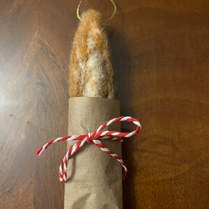 May include: A brown and white felted ornament wrapped in brown paper and tied with red and white twine.