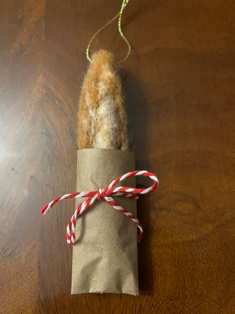 May include: A brown and white felted ornament wrapped in brown paper and tied with red and white twine.