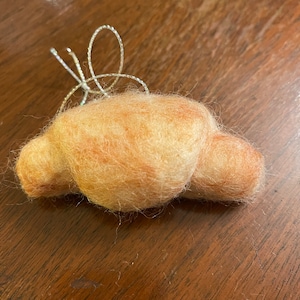 May include: A light brown felt croissant with a silver wire ornament on top.