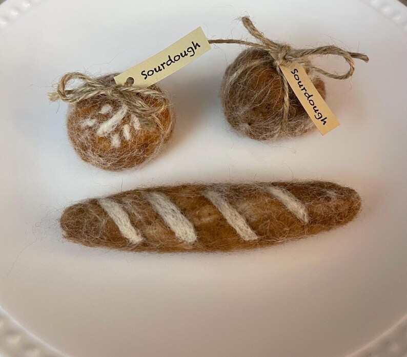 May include: Two brown felt balls with the word "Sourdough" written on small tags, and a brown felt baguette with white stripes.
