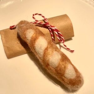 May include: A hand-felted brown and white baguette with a red and white twine bow tied around it.