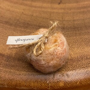 May include: A small, round, light brown object tied with twine, with a white tag that reads "sourdough". The object has a textured, fuzzy appearance. The image is taken from a close-up angle.