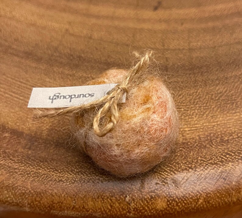 May include: A small, round, light brown object tied with twine, with a white tag that reads "sourdough". The object has a textured, fuzzy appearance. The image is taken from a close-up angle.
