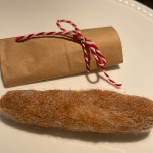 May include: A brown felt sausage wrapped in brown paper with a red and white twine bow.