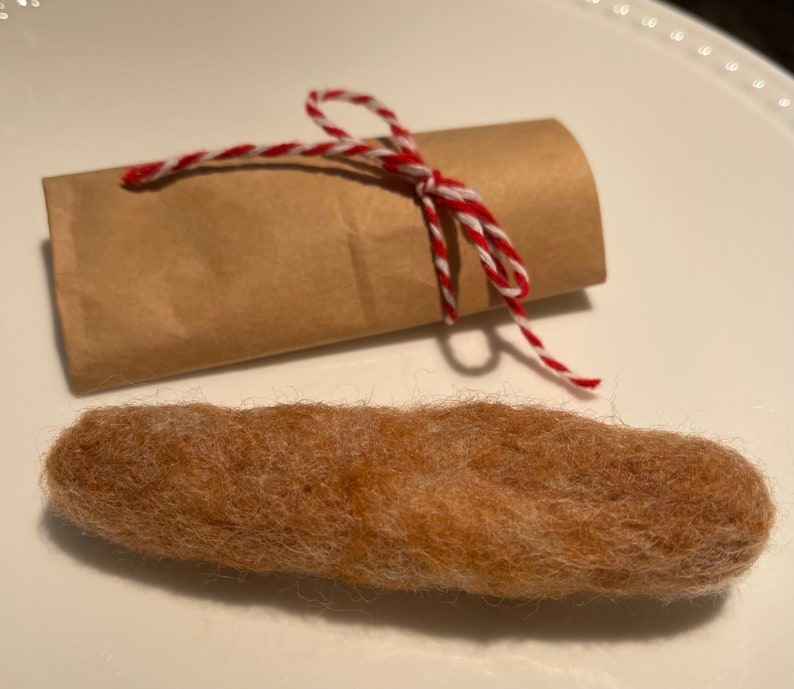 May include: A brown felt sausage wrapped in brown paper with a red and white twine bow.