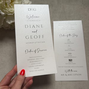 May include: Two white wedding program cards with black text. The left card reads Welcome to the wedding of Diane and Geoff, Saturday 22nd July 2026, Order of Service. The right card lists the Order of the Day with icons for events and times.