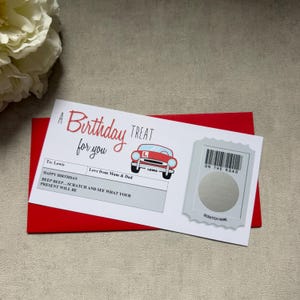 Peut inclure: Une carte d'anniversaire rectangulaire blanche avec le texte rouge A Birthday TREAT for you, une illustration de voiture rouge avec un panneau L, et une zone à gratter grise marquée ON THE ROAD. La carte est posée sur une enveloppe rouge.
