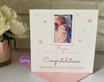 May include: A white greeting card with a photo of a baby girl, pink hearts, and stars. The card reads "Congratulations" and includes the baby's name, birthdate, and weight. A pink envelope is visible.