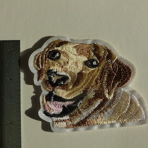 May include: Embroidered patch of a brown and white dog with a pink tongue sticking out. The dog is looking to the right. The patch is on a white background.